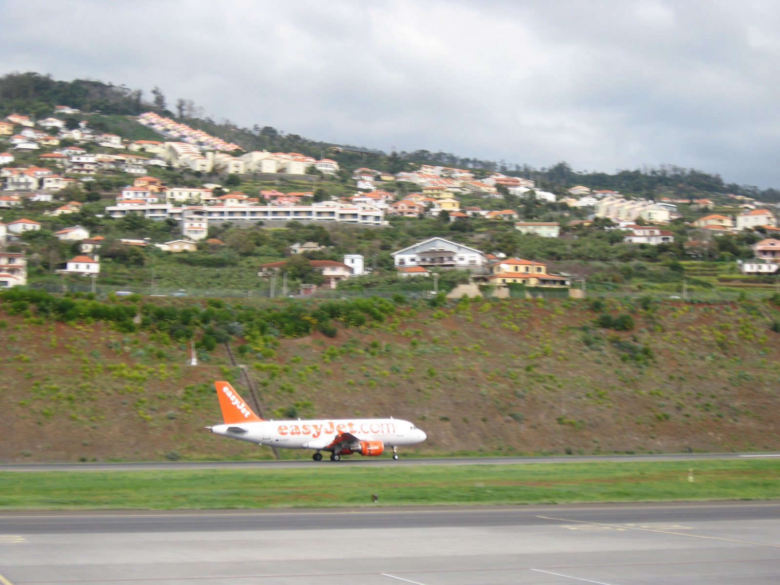 Un Airbus A319 se pose sur la piste de l’aéroport de Madère, derrière lui les coteaux en terrasses et les maisons pastel de Santa Cruz montant à pic.