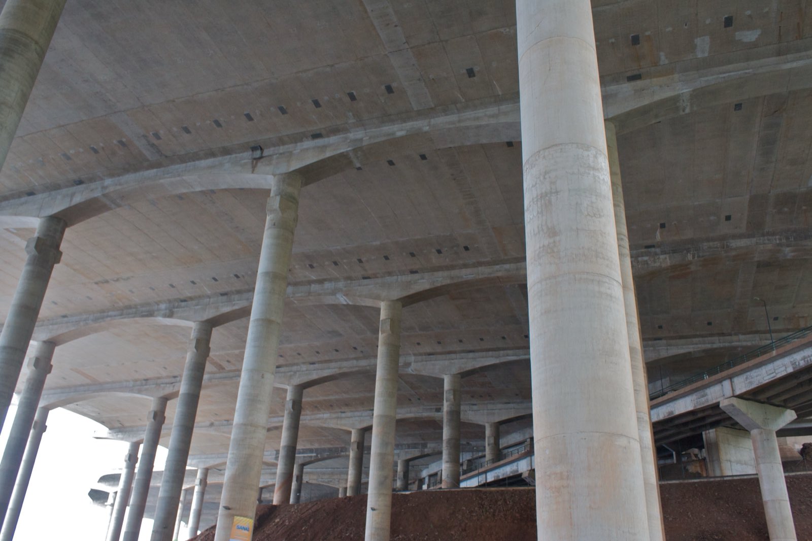 Vue du sol vers la forêt de colonnes de béton qui soutient le tablier de la piste de l’aéroport de Madère, le dessous du tablier occupant le haut du cadre.