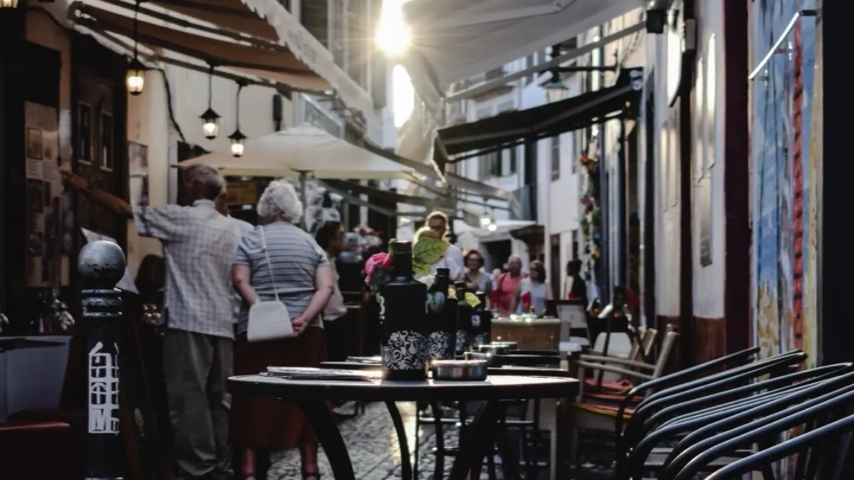 Restaurant tables, chairs and people filling a narrow cobbled lane in Funchal’s Old Town, with awnings overhead and painted panels along one wall.